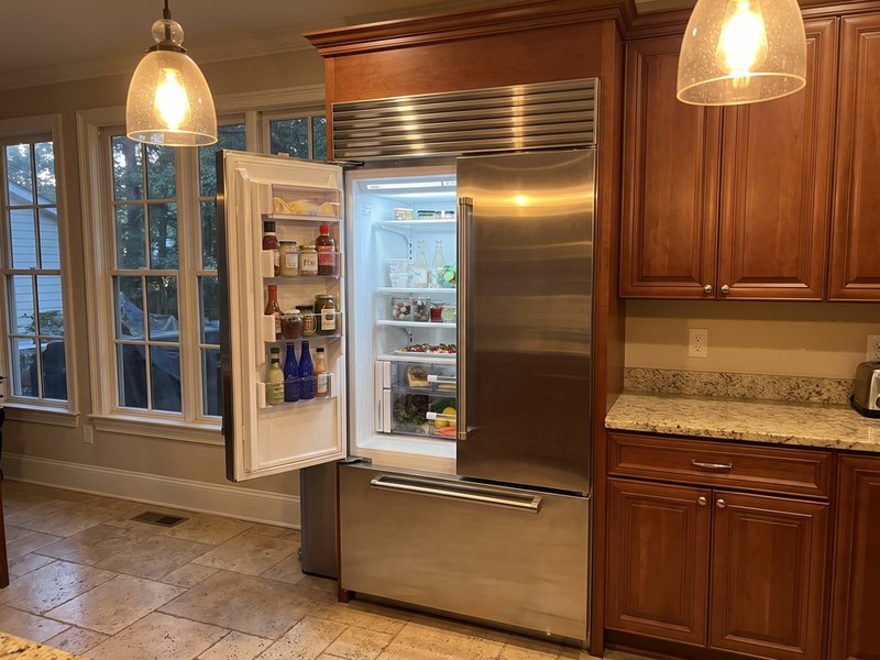 Built-in stainless steel refrigerator with one door open in a wood-cabinet kitchen